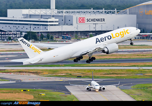 Bird-like perspective, looking down on the departing Triple7 and a LOT Embraer jet about to cross runway 25C. Buildings of freight-fowarder DB-Schenker in the background. Boeing 777-FZN
